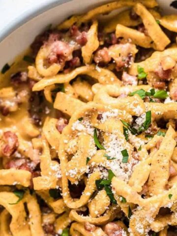 Pasta Carbonara inside a bowl with herbs and bacon.