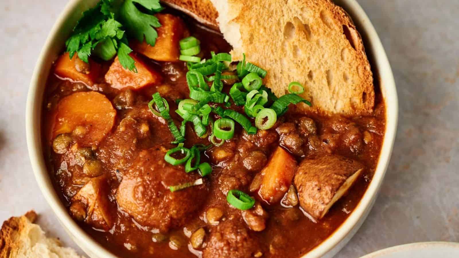 A bowl of stew with bread and carrots.