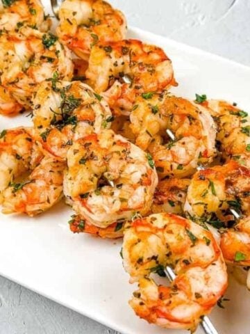 Shrimp skewers on a white plate with lemon wedges.