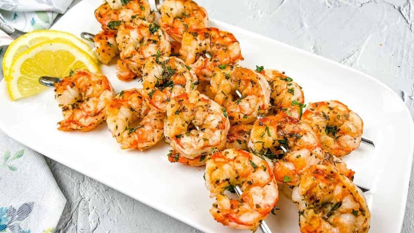 Shrimp skewers on a white plate with lemon wedges.