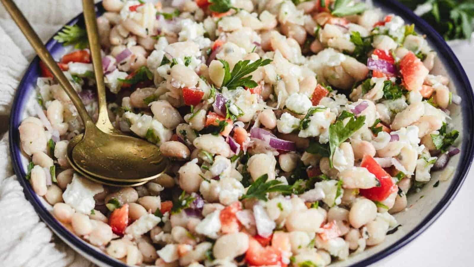 Side view of white bean salad in bowl with tongs.