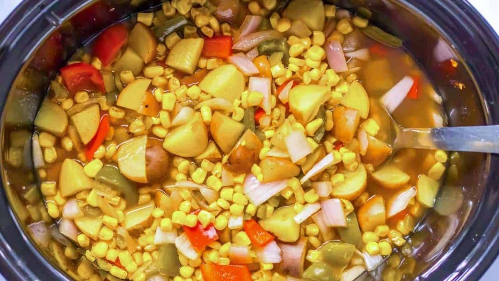 Street corn soup with potatoes, corn and red pepper in the crock pot with a spoon on the side.