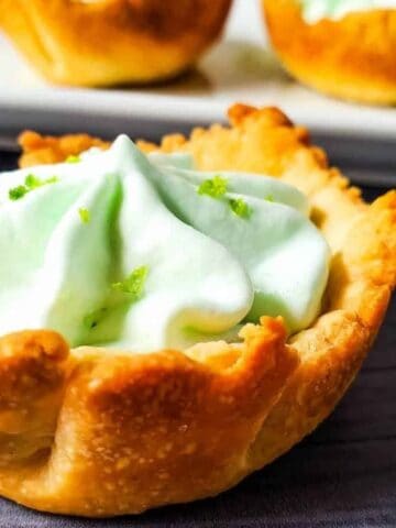 A front view of a mini key lime pie with more on a white plate in the background.