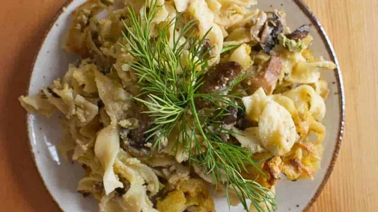 A plate of pasta with mushrooms and sprigs of dill.