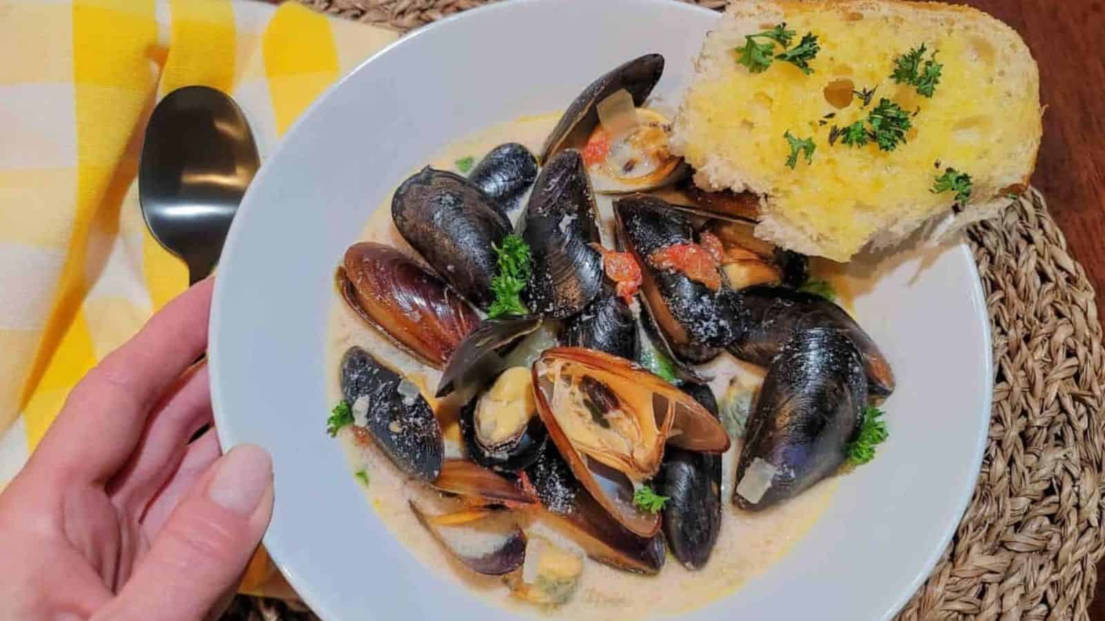 A person holding a bowl of steamed mussels.