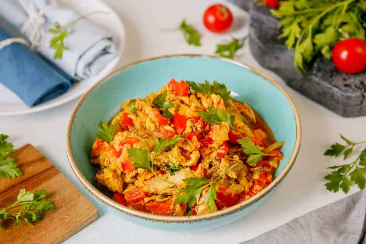 A bowl of Nigerian egg stew food with tomatoes and herbs on a table.