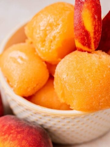 A bowl of perfect peach sorbet with fresh peaches.