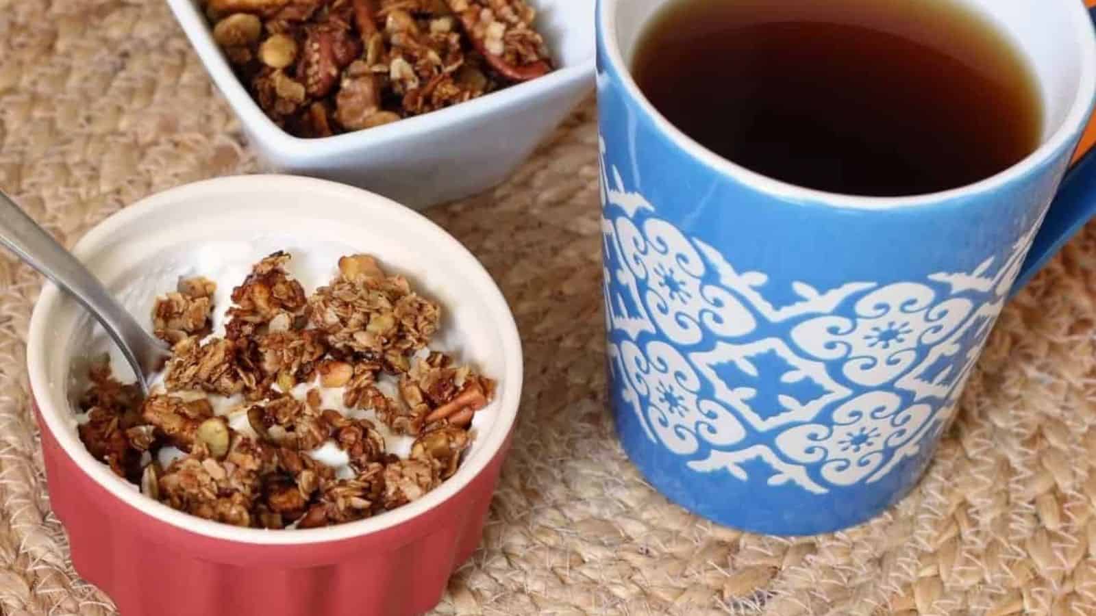 Bowl of yogurt topped with granola next to a cup of coffee.