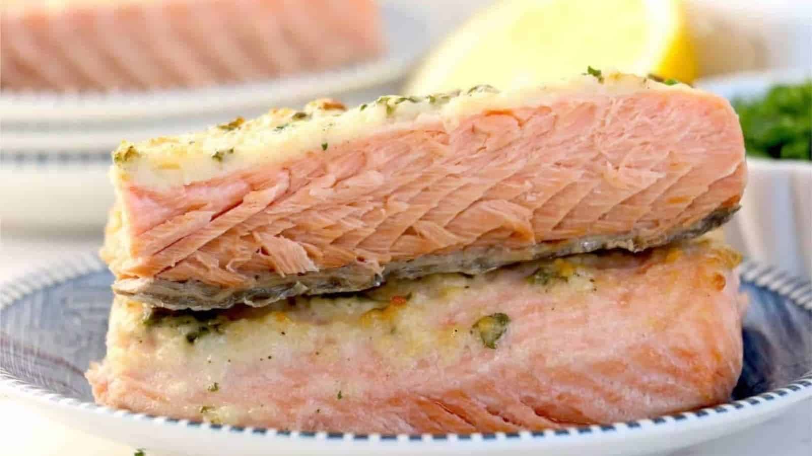 Salmon fillets stacked on a plate with lemons and herbs in the background.