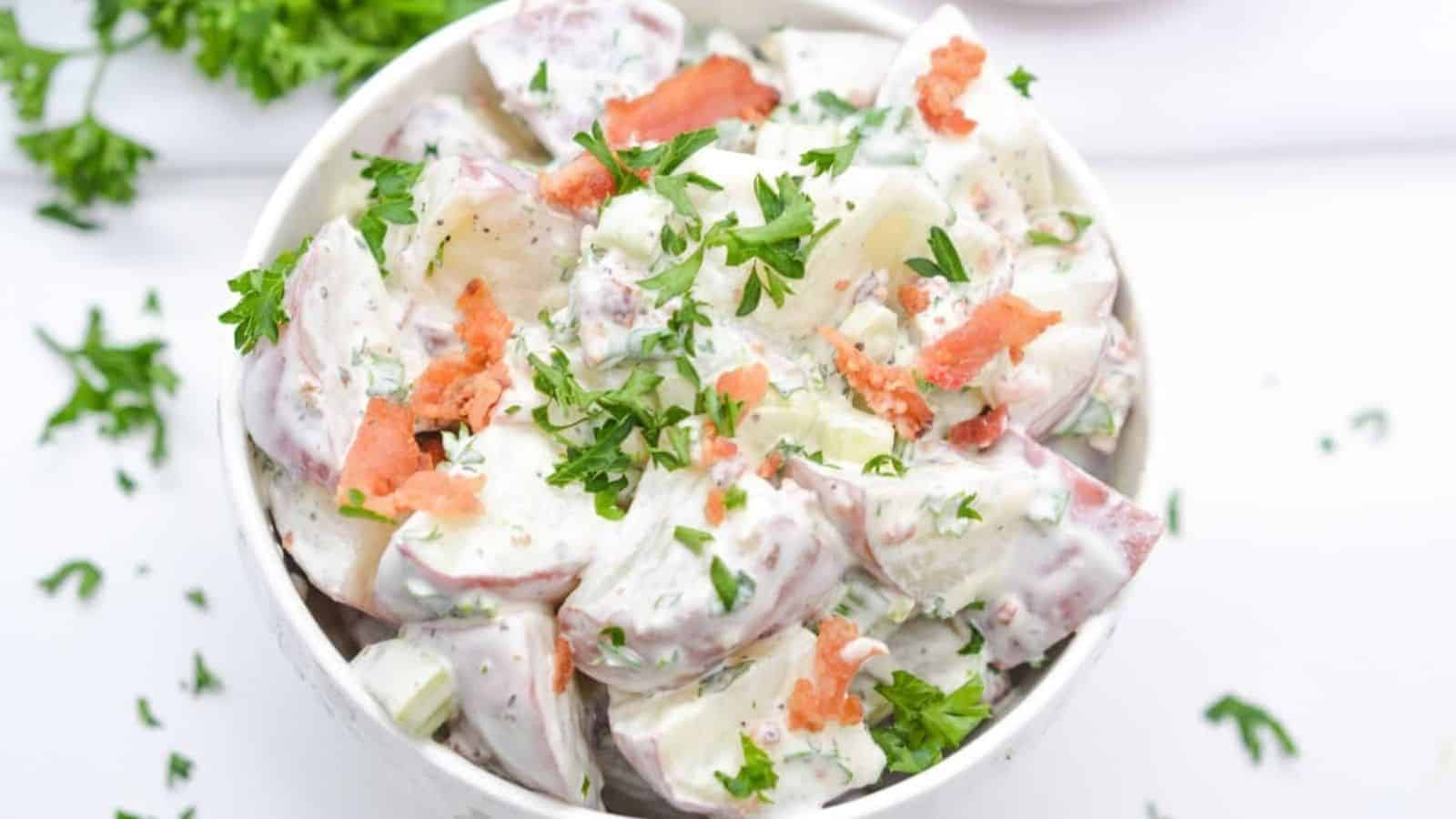 Red potato salad in bowl with bacon and parsley garnish.