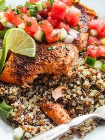 A white plate with quinoa, arugula, and roasted salmon topped with a watermelon and cucumber salsa.