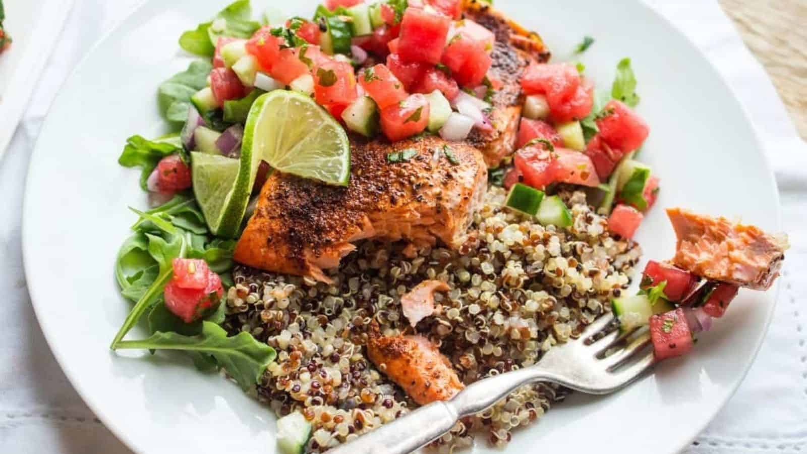 A white plate with quinoa, arugula, and roasted salmon topped with a watermelon and cucumber salsa.