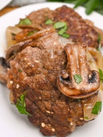 A cooked meatloaf topped with sliced mushrooms and garnished with parsley on a white plate.