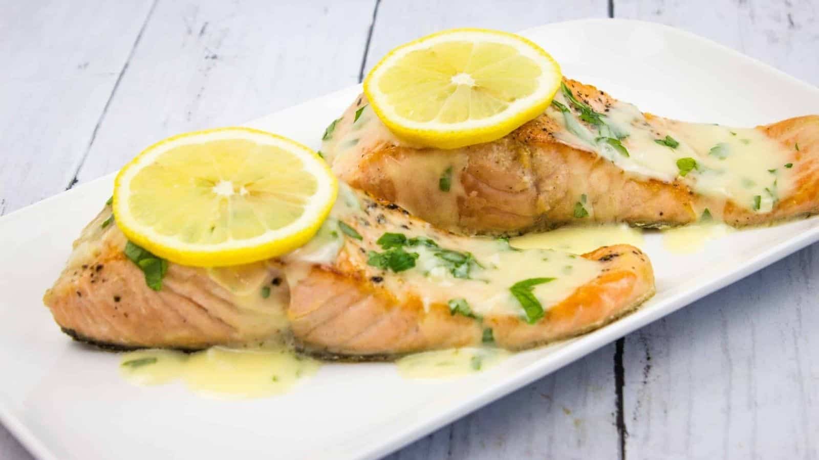 Two salmon fillets with lemon sauce on a white plate.