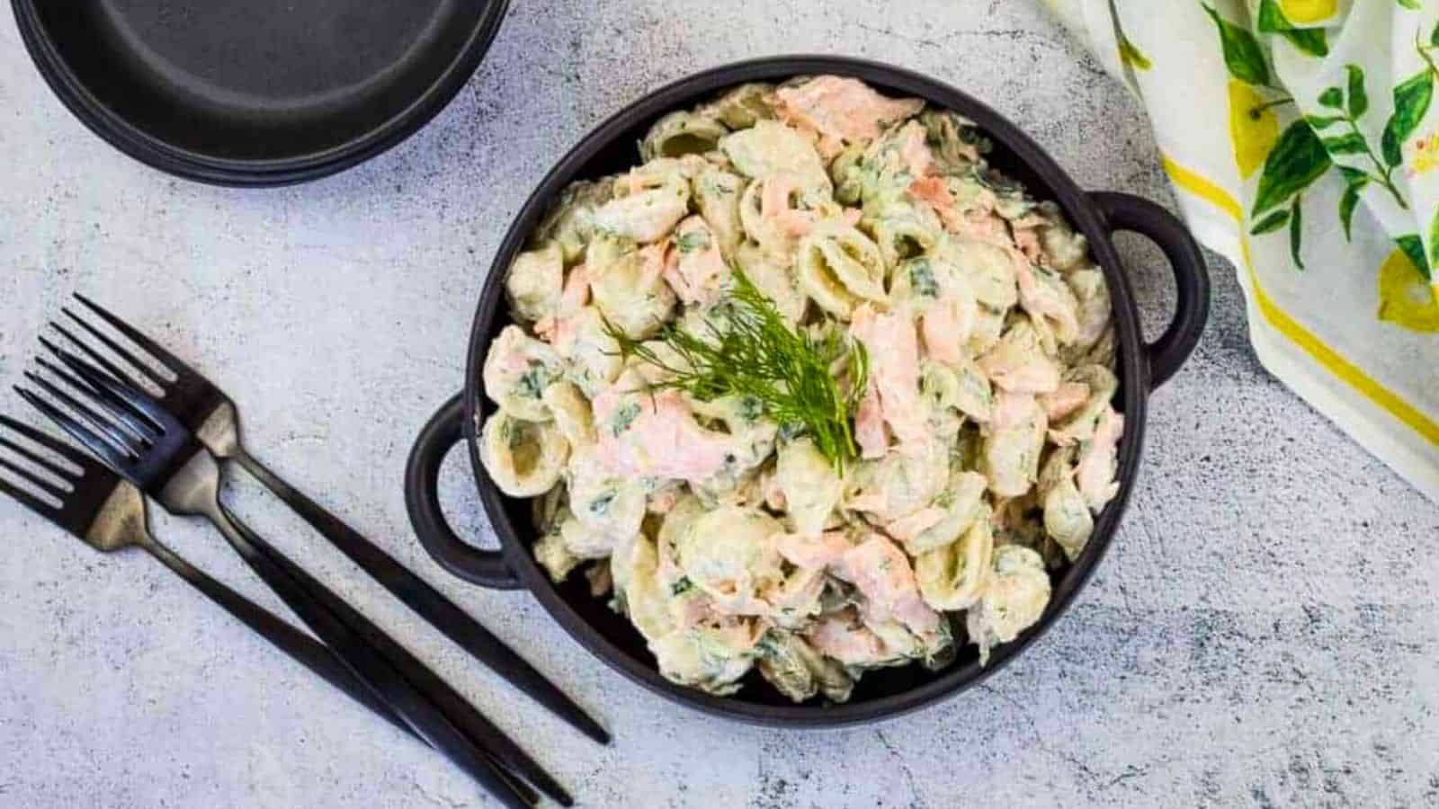 Salmon pasta salad in a black bowl with forks nearby.