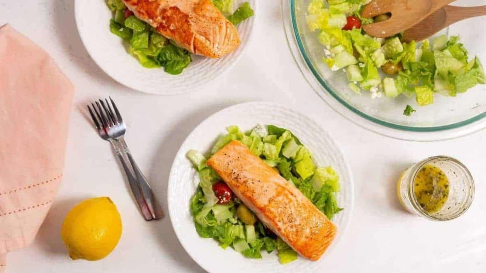 Salmon salad on white plates and lettuce greens in a bowl.