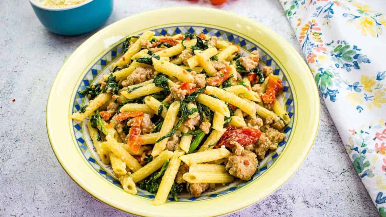 Broccoli Rabe and Sausage in a serving bowl with tomatoes in the background.