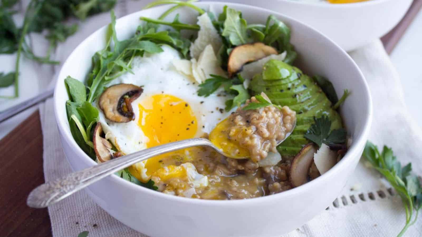 A bowl with oatmeal topped with avocado, mushrooms, arugula, and a fried egg.