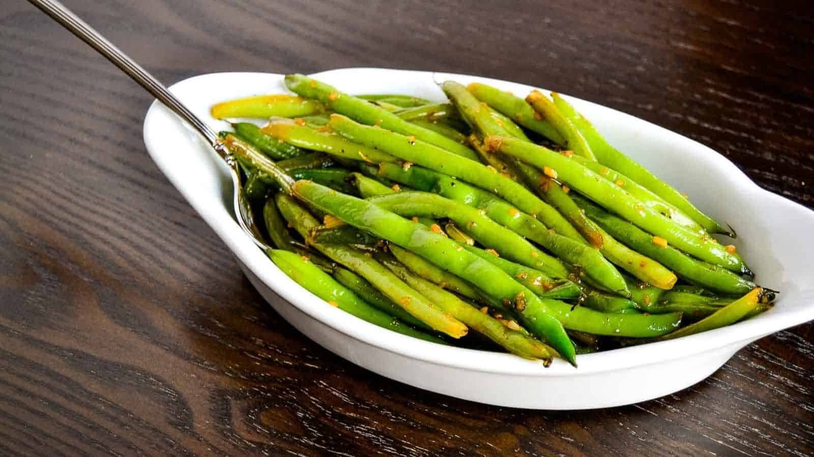 Screaming skillet green beans in a white bowl on a wooden table.