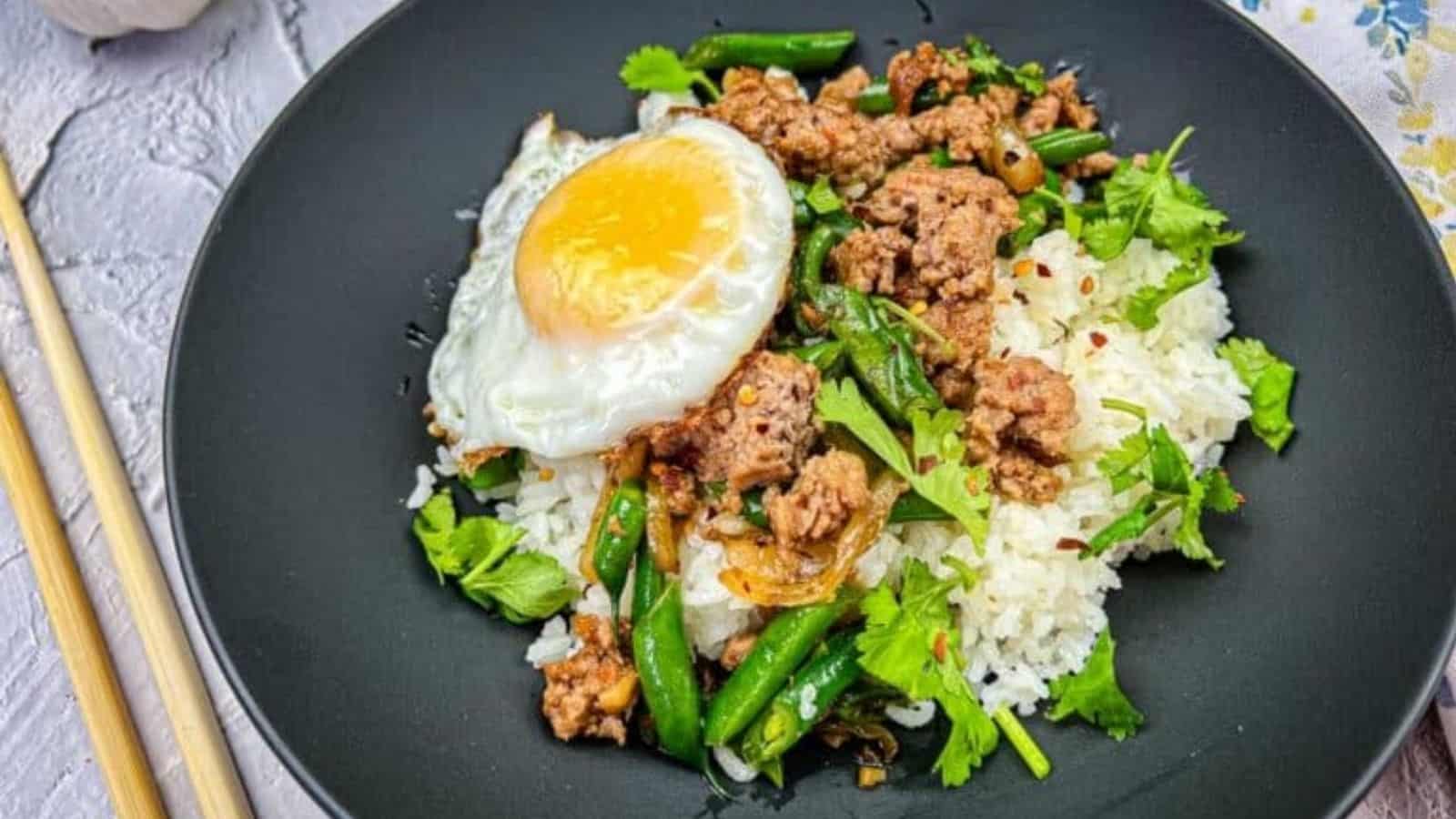 Overhead view of sizzling Thai pork green beans on a Blackstone griddle with a fried egg on top.