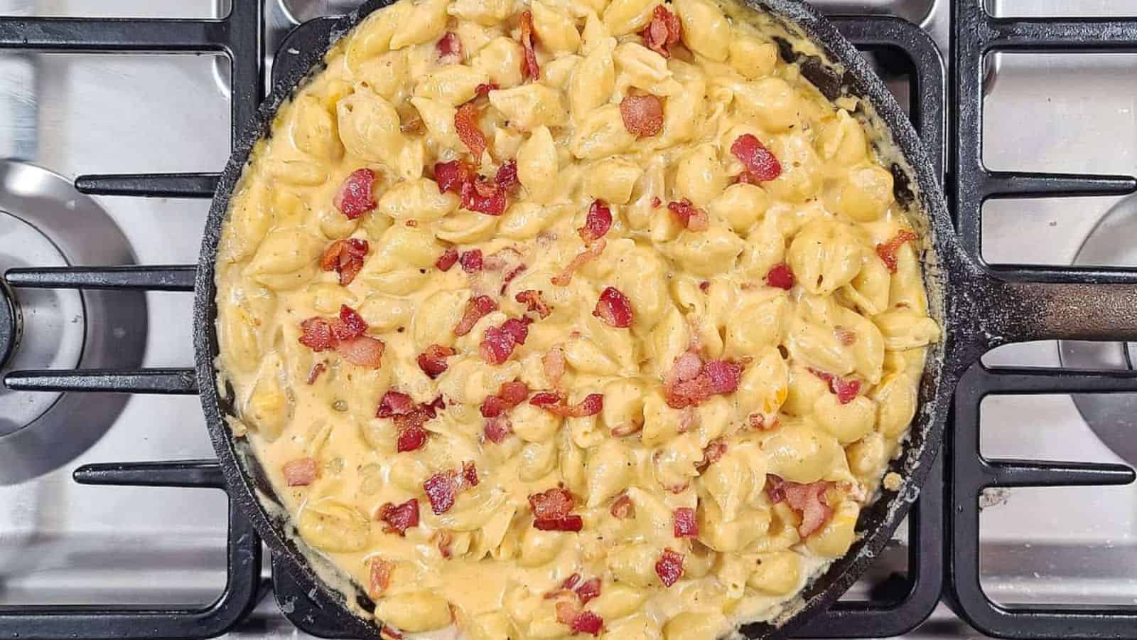 A skillet filled with smoked mac and cheese and bacon on a stove top.