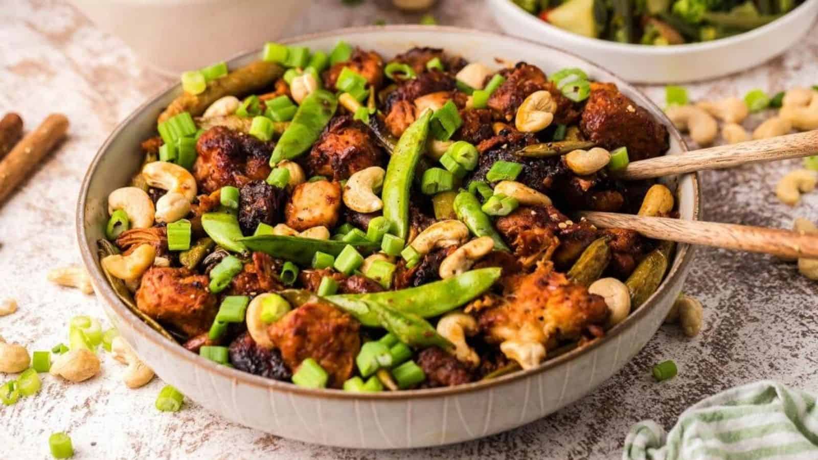 Slow cooker cashew chicken with wooden utensils in a bowl.