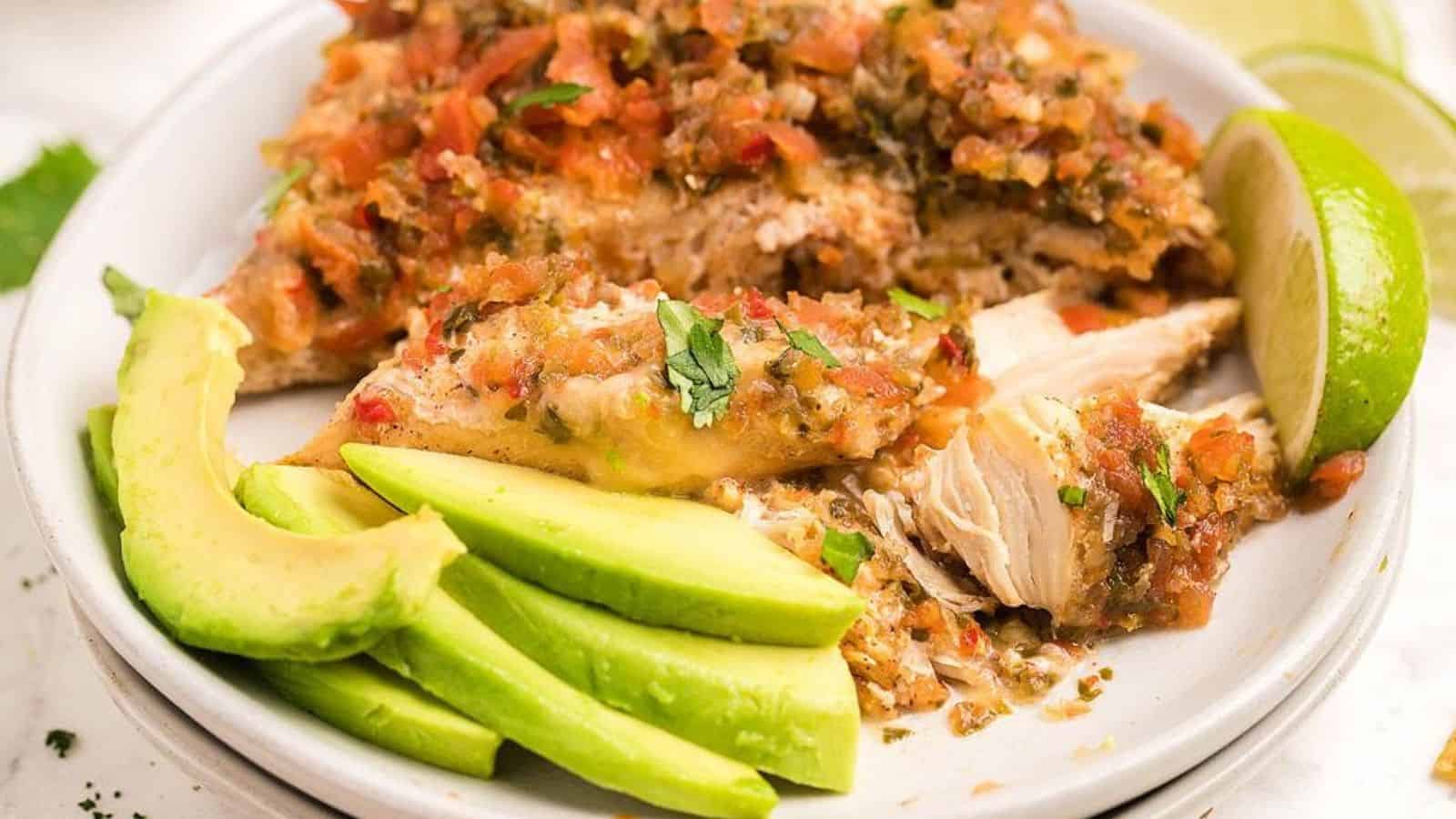 Slow cooker salsa fresca chicken with slices of avocado and lime in a white plate.