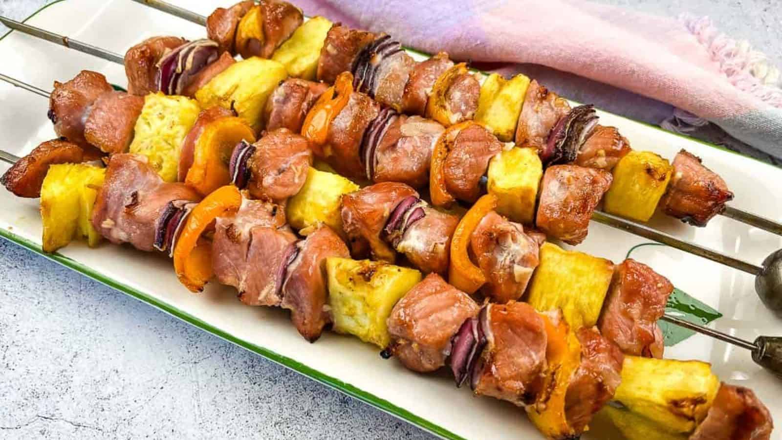 Four smoked pork and pineapple skewers on a wooden board.
