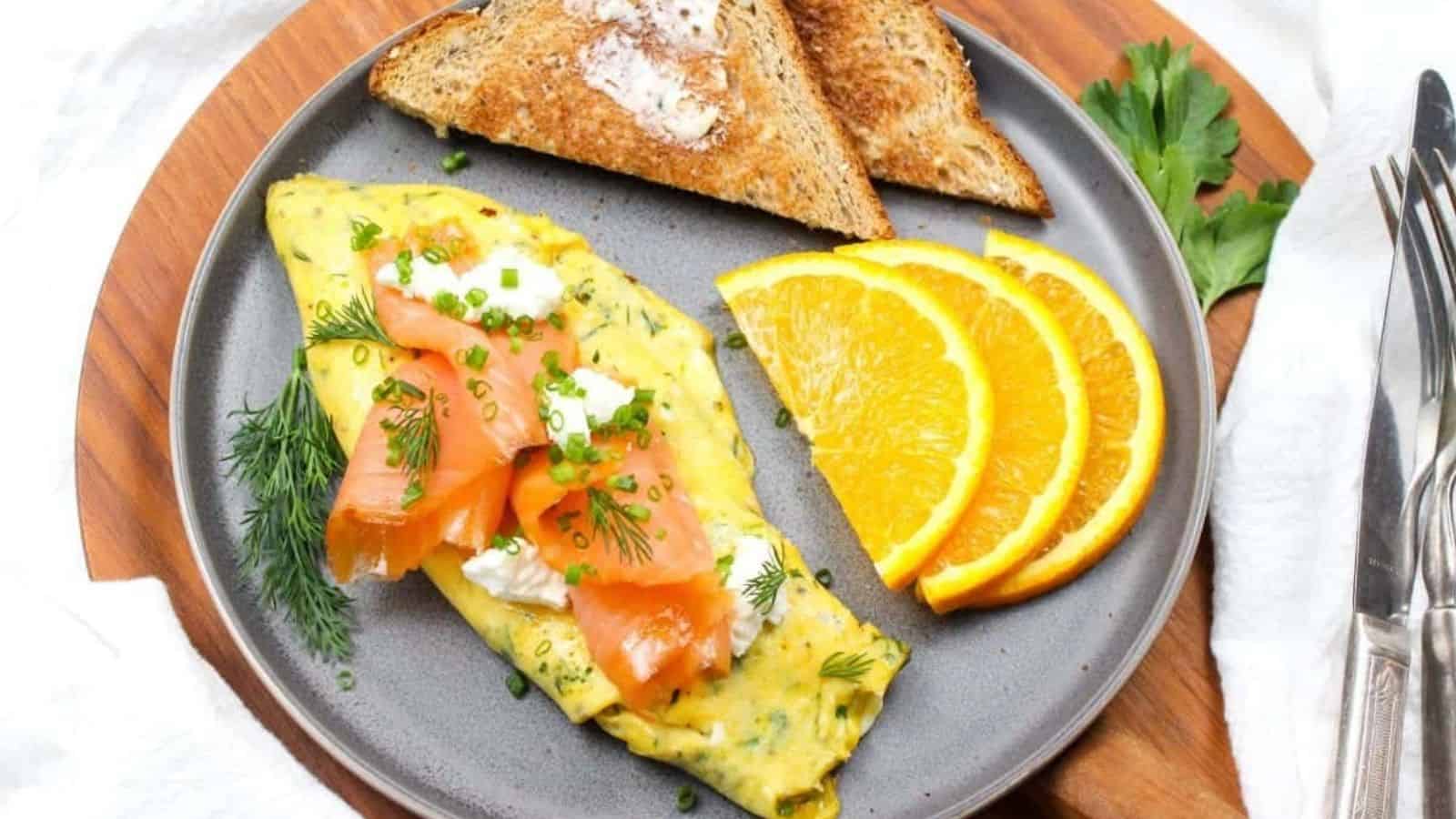 An omelette with smoked salmon and goat cheese on a plate with toast and orange slices.