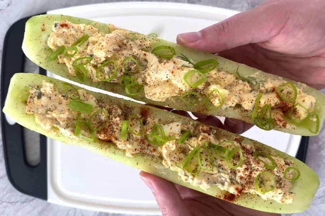 Spicy egg salad cucumber boats being held in hands.