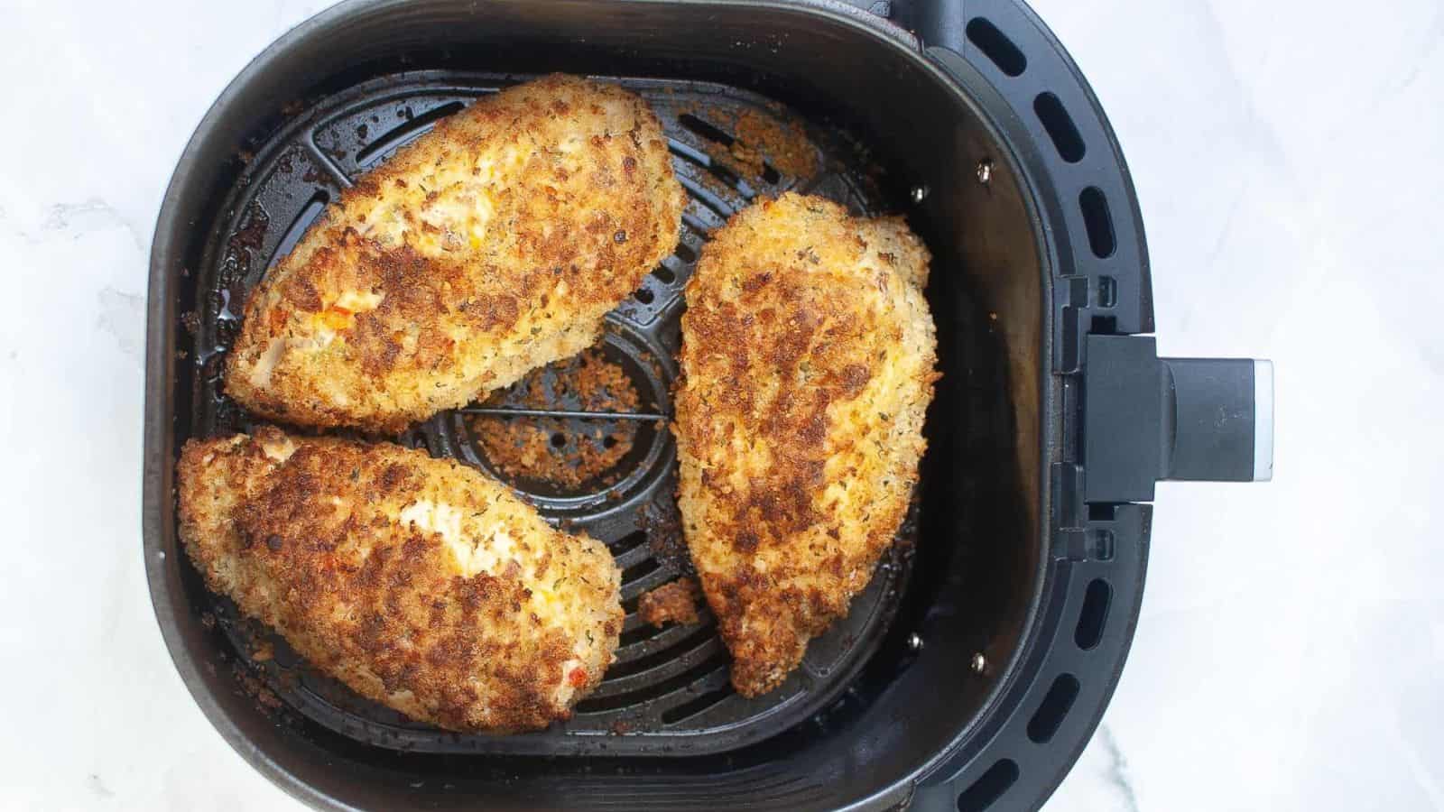 An air fryer basket with stuffed chicken breasts.