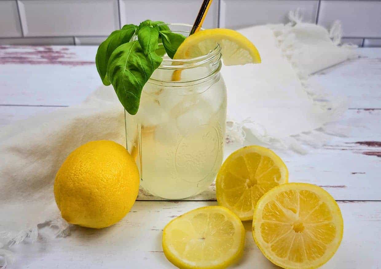 Freshly squeezed sugar free lemonade in a mason jar with lemon slices and basil leaves.