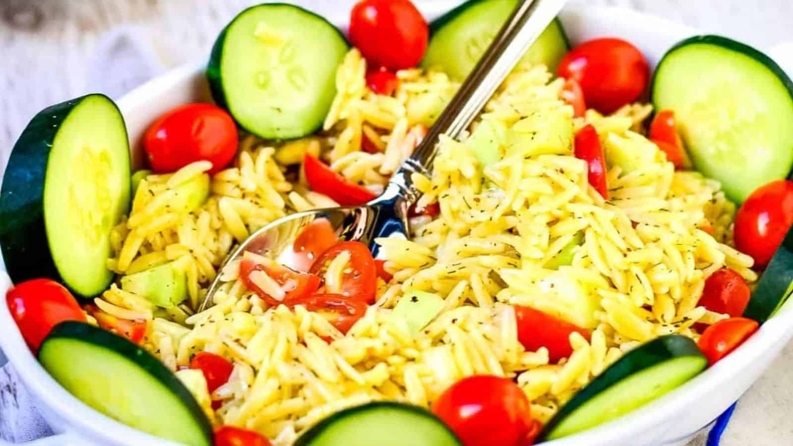 Summer orzo pasta salad in a while serving bowl on a whitewashed background next to a bowl of green beans.