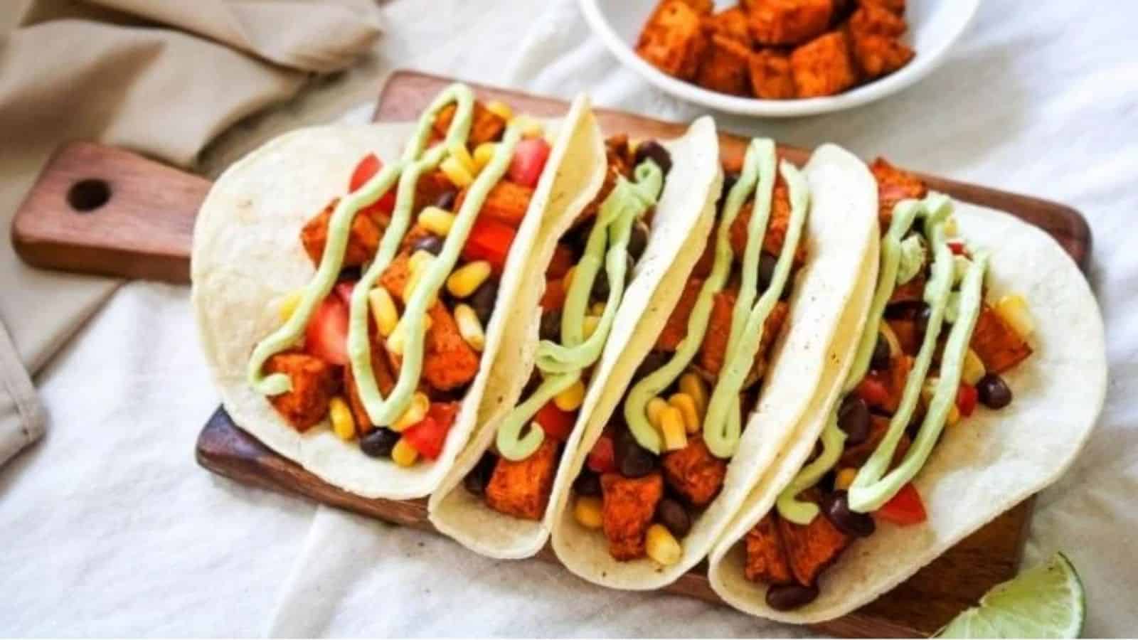 Close-up of four sweet potato and black bean tacos on a wooden bord.