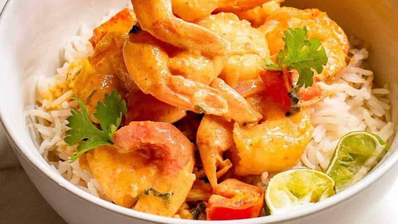 Overhead shot of a bowl of Thai shrimp curry over rice with silverware and lime wedges on the side.