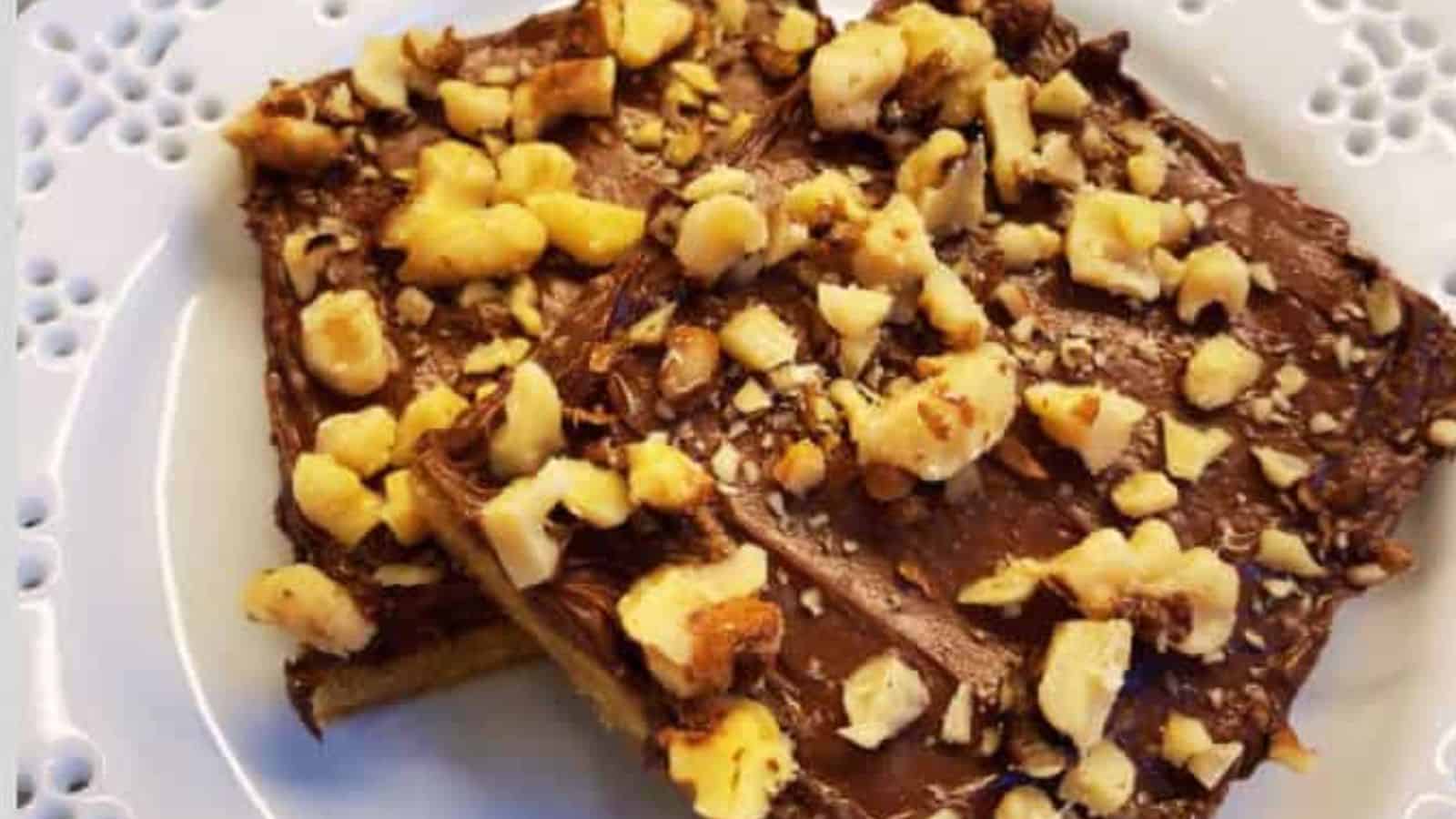 Two toffee cookies on white plate with bowl of chocolate chips in background.