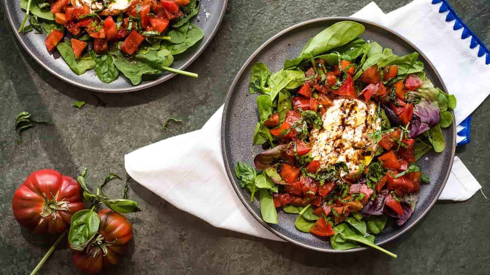 An assembled tomato burrata salad with sliced basil and burrata on a cutting board and a bowl of chopped heirloom tomatoes.