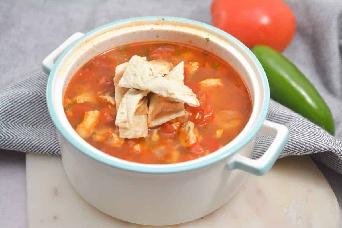 Tortilla soup in a white bowl on a cutting board.