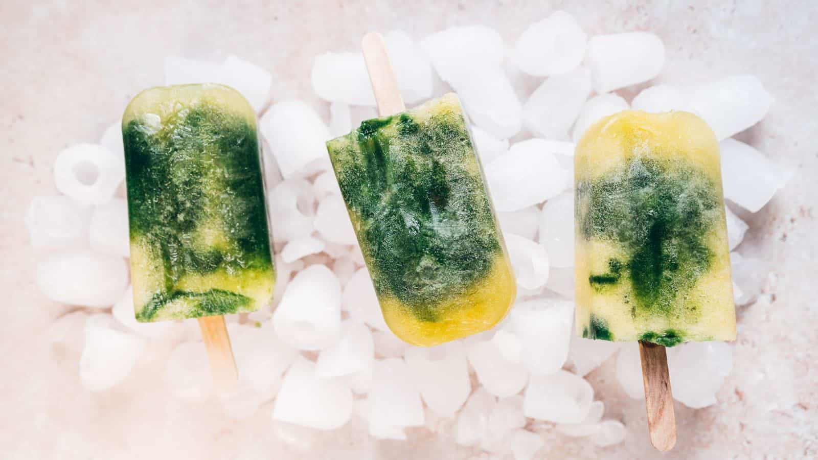 Three tropical green smoothie popsicles on ice.