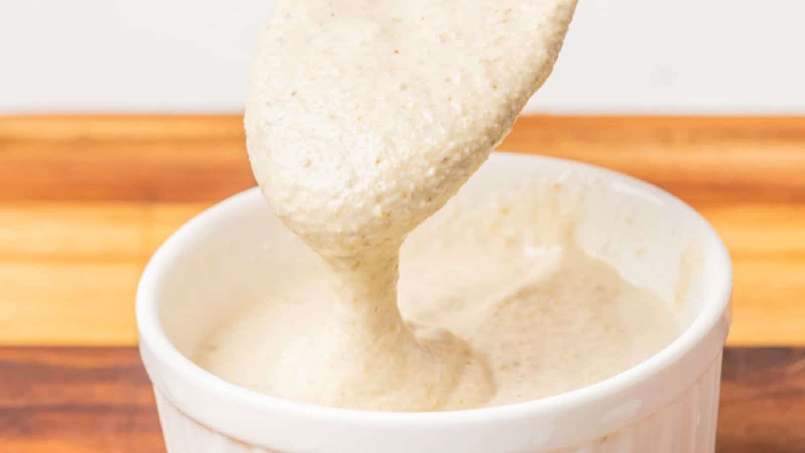 Close-up image of a caesar salad dressing in a small bowl with a spoon scooping a spoonful of it.