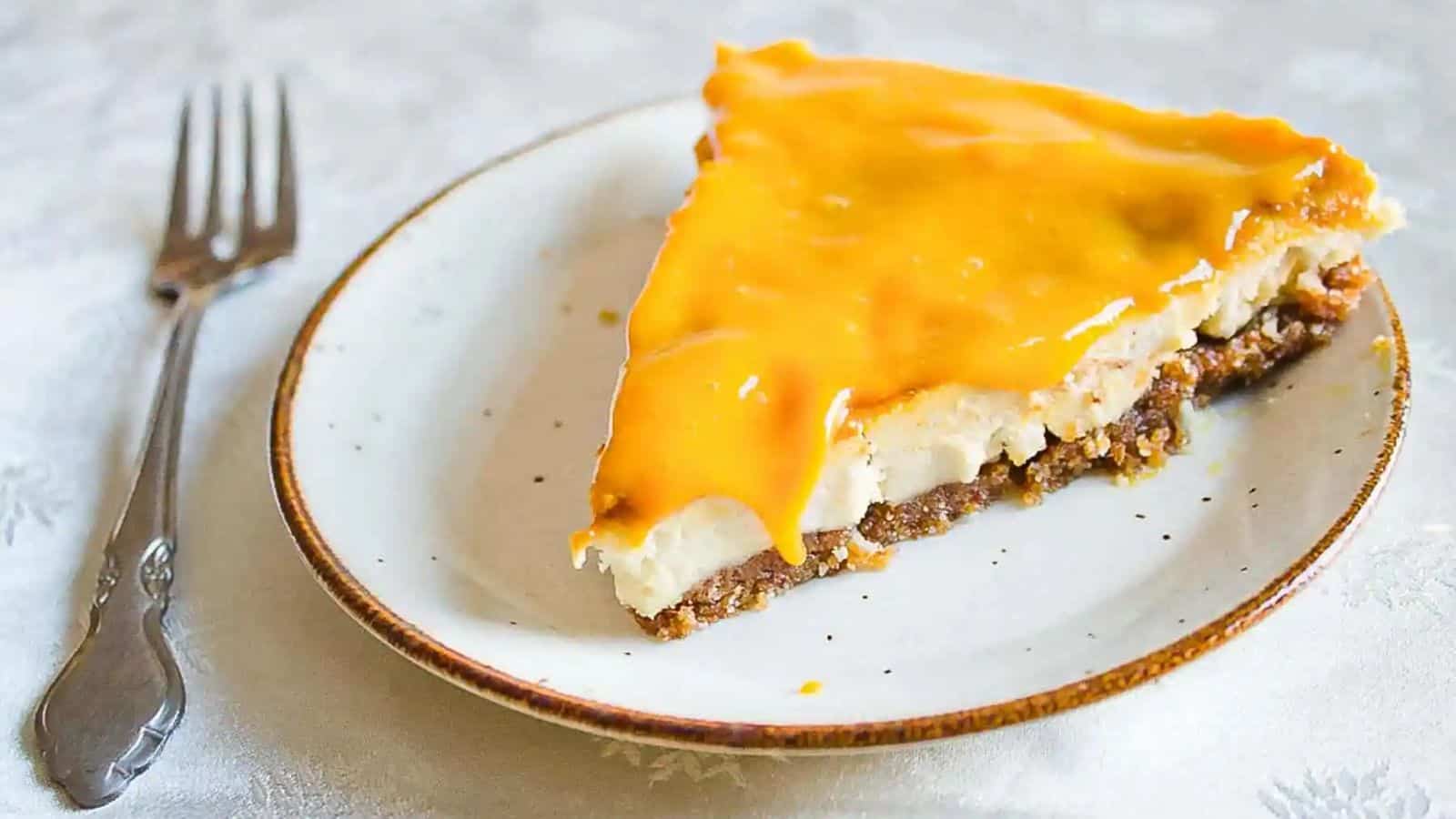A slice of vegan mango cheesecake on a plate with a fork.
