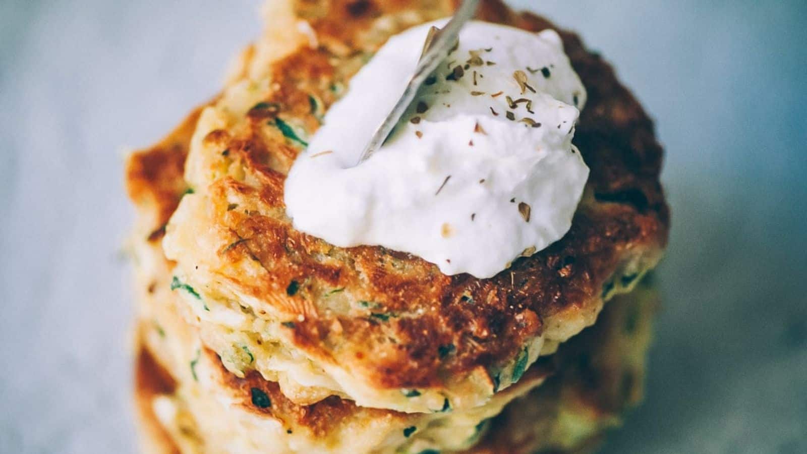 A stack of vegan zucchini fritters on a plate with cream cheese frosting on top.