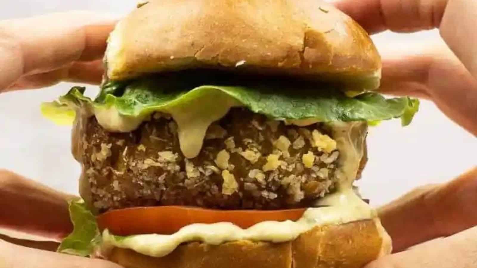 Close-up image if hands holding a burger with vegan chicken pattie.