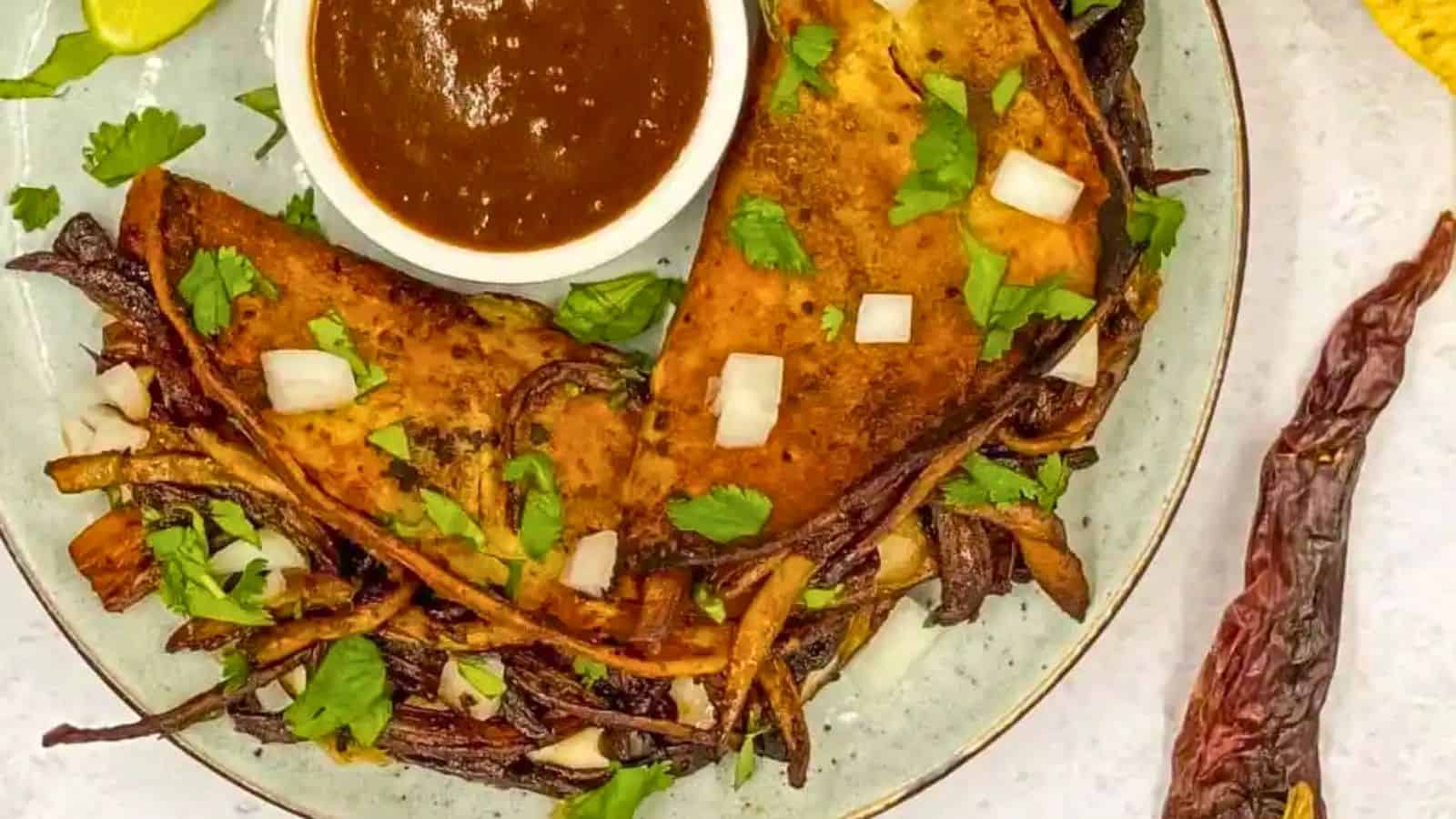 Overhead of 2 vegetarian birria tacos (quesabirria) with sauce in a plate.