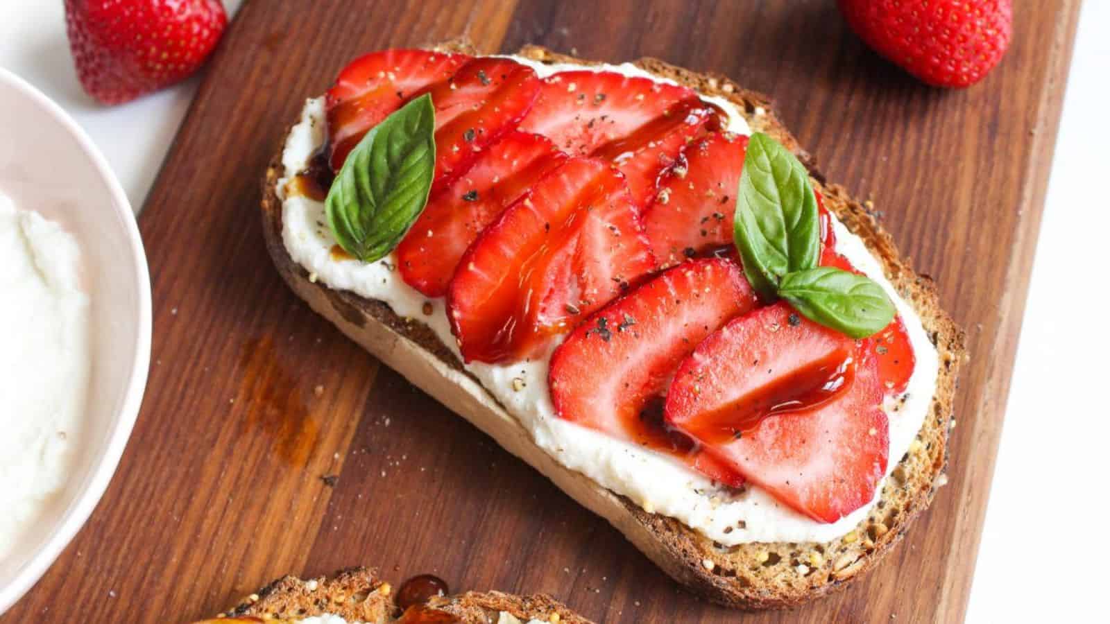 A slice of toast with sliced strawberries and ricotta cheese on top.