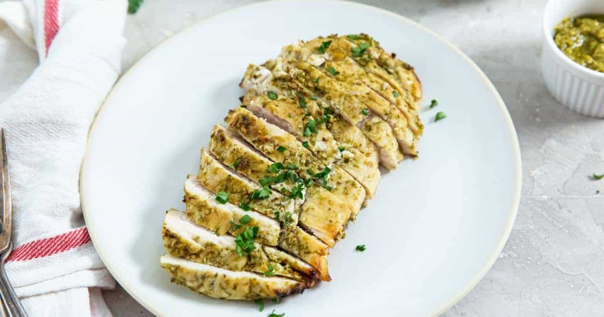 Easy Air Fryer Pesto Chicken Breast with parsley on a white plate.