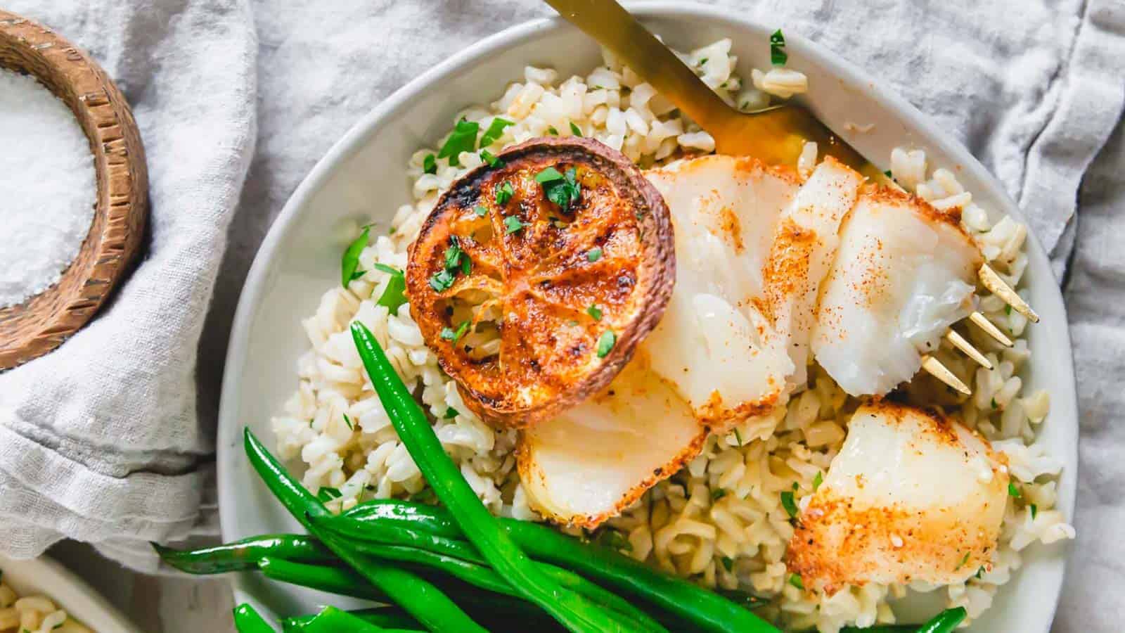 Air fryer cod on a plate with green beans and rice.