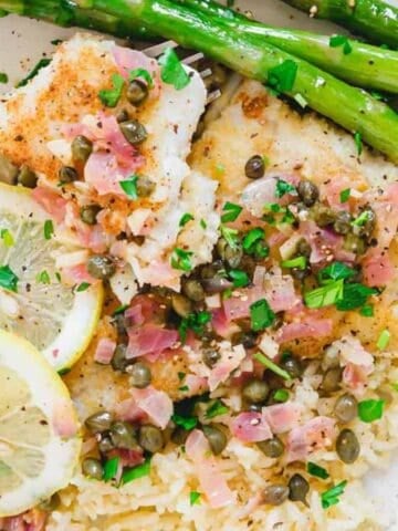 Cod piccata on a plate with asparagus and rice.