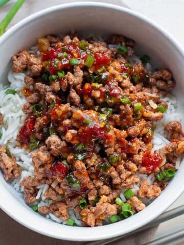 A white bowl with rice and hoisin ground beef and chopsticks on the side.