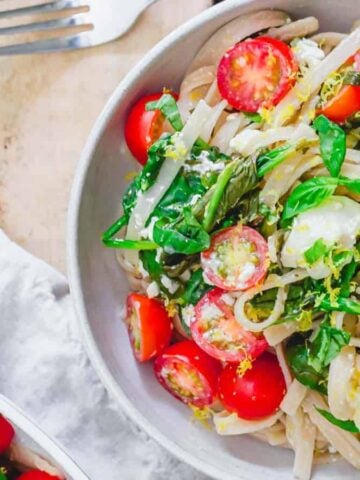 Lemon pasta with spinach, feta and cherry tomatoes in a bowl.